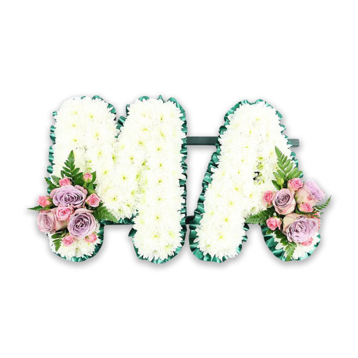 This detailed funeral tribute features the word MA crafted in large, capital letters, designed as a deeply personal farewell for a mother or someone known affectionately as Mama. Each letter stands sturdy and full, its entire surface covered with dozens of pristine white chrysanthemums arranged so close together that no gaps show between the blooms. Their petals overlap like tiny, soft feathers, giving the letters a pillowed, almost quilted texture. The outer edges of the M and A are finished with a luxurious band of rich emerald green ribbon, folded into fine pleats that run continuously along every edge. This dark green frame brings structural clarity and a sophisticated contrast to the pure white flowers. A discreet bar of foliage connects the letters from behind, keeping them aligned and forming a cohesive, balanced design. At the lower left corner of the M and the lower right side of the A, two symmetrical sprays of pastel flowers introduce colour in a gentle, controlled way. Soft lavender roses, pale pink roses, and tiny pink spray rose buds cluster together, their velvety petals unfurling at different stages of bloom. Each posy is embellished with a single arching fern frond, its delicate leaflets adding light texture and echoes of a peaceful garden in Canonbury Square. The entire tribute is photographed against a simple white background, allowing every blossom, ribbon fold, and stem to stand out clearly. Perfect for a funeral or memorial service, this bespoke letter arrangement speaks of tenderness, gratitude, and lasting remembrance, reflecting the thoughtful work of a skilled local Canonbury florist.