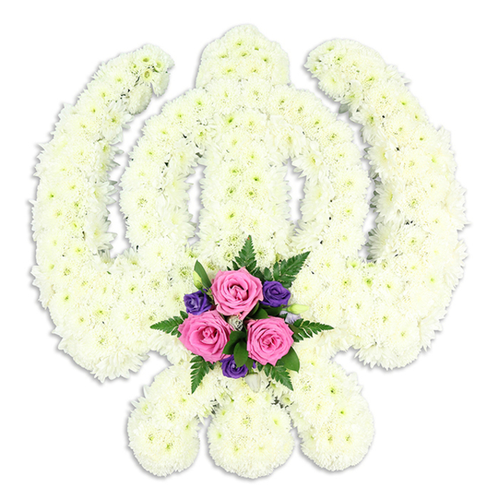 A stately Khanda-shaped floral tribute fills the frame, its sacred Sikh emblem rendered with meticulous care in pure white blossoms against an immaculate white background. The central sword, or khanda, rises vertically with clean, defined edges made entirely of closely packed chrysanthemum heads, each bloom overlapping in a way that softens the strong lines while preserving the clarity of the symbol. Surrounding this sword, the chakkar forms a perfect ring of white petals, creating the sense of an unbroken circle of light. At the base, the two kirpans sweep outward, their curved forms outlined by the same cushiony flowers, giving the entire composition a balanced and harmonious shape. The chrysanthemums are fresh and full, their almost feathery petals creating a velvety, tactile impression that suggests a quiet, comforting presence. Nestled where the kirpans cross at the lower centre is a carefully composed cluster of accent flowers, drawing the eye with gentle colour rather than overpowering brightness. Three pink roses sit at the heart of this cluster, their petals spiralling in tight yet generous blooms, with hues ranging from dusty rose to soft shell pink. Around them, rich purple blossoms, possibly lisianthus or small freesias, introduce a deeper note of colour that feels dignified and serene. Lush green fern fronds and foliage weave through and around this group, their slightly glossy leaves catching the light and adding movement to the design. The tribute is lit evenly, with a faint shadow below hinting at its three-dimensional structure, as if it were resting on a table in a quiet Canonbury home or near the peaceful streets around Upper Street. This bespoke floral Khanda would be chosen by local families for Sikh funeral services or memorials, a meaningful blend of tradition, faith, and floral artistry that speaks softly of remembrance and respect.
