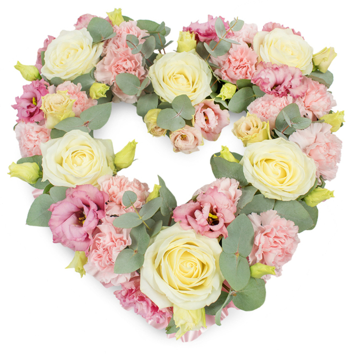 This image shows a large, heart-shaped funeral tribute made entirely of soft, pastel flowers and delicate foliage, set clearly against a bright white background that lets every detail stand out. The heart form is precise and complete, with no gaps, its entire surface covered in layered petals that feel almost like fabric. The most striking blooms are the cream and pale yellow roses, placed at balanced intervals so the eye naturally travels around the heart's outline. Their petals are full and velvety, unfurling from tight centres into graceful, rounded heads that suggest purity, loyalty, and deep respect. Around and between these roses sit clusters of pale pink carnations, their frilled petals forming small, textured mounds that fill out the design and make it appear especially lush. Interspersed among the pastel tones are richer pink and mauve lisianthus, whose open, softly curled petals and occasionally darker centres add contrast and a quiet depth, like gentle shadows among the lighter flowers. Tiny, still-closed yellow-green buds shimmer here and there, completing the sense of freshness and careful timing. Silvery-green eucalyptus leaves snake gracefully through the arrangement, their smooth, rounded shapes and muted tones giving the wreath a soothing, almost aromatic quality you can imagine breathing in. The mood is reflective and compassionate, evoking the hushed atmosphere of a farewell service at a Canonbury church or a thoughtful gathering after a funeral near Upper Street. This heart-shaped wreath feels like a tender, handcrafted expression of sympathy and remembrance, the kind of design a trusted Canonbury florist would prepare with particular care for a much-loved relative or friend.
