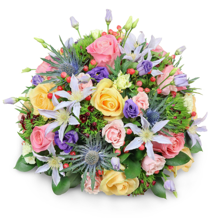 Set against a seamless white background, this domed bouquet appears almost to hover, its rounded shape casting a gentle shadow that emphasises its fullness and expert construction. The design is rich with flowers and foliage, layered so that colours and textures mingle like a carefully painted canvas, much like the curated borders you might find near Canonbury Gardens. At its centre and flowing outward, garden roses in soft pink, mellow yellow, and creamy peach offer a romantic foundation. Some roses are completely open, revealing tight spirals of velvety petals, while others remain half-closed, suggesting freshness and longevity. Threaded through this rosy base are clematis flowers with starry, open faces, their petals tinted in pale lavender and white, each bloom featuring a clear yellow or creamy centre that brings a gentle light to the arrangement. Punctuating the softness are bold stems of blue eryngium, or sea holly, with spiky, thistle-like heads in metallic blue-grey, adding a contemporary structure that feels as though it was inspired by the wild edges of a North London park. Smaller, cup-shaped lisianthus in deep purple and hints of pale green nestle among the larger blooms, filling out the spaces while creating subtle shifts in tone. Scattered throughout are bright red hypericum berries, clustered like tiny beads, providing a cheerful burst of colour and a firm, glossy texture against the velvety petals. A generous collar of foliage frames the bouquet, from broad, shiny green leaves to soft, feathery sprigs and occasional darker, burgundy-tinged greens, giving depth and a natural, garden-grown character. The result is an arrangement that feels sophisticated yet welcoming, ideal for a thoughtful delivery to a Canonbury home, whether to celebrate, console, or simply bring the feeling of a blooming garden indoors.