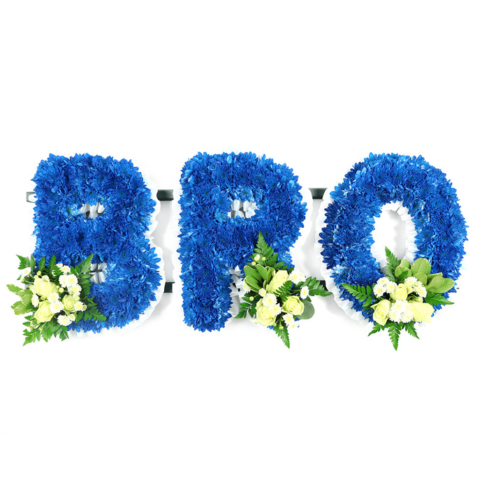 A studio photograph, taken at eye level against a pristine white background, shows a three-piece funeral tribute spelling the letters B, R and O in strong, capital forms. Each letter is constructed from tightly packed royal blue chrysanthemum florets, their small, rounded heads creating a luxurious, textured surface that holds crisp outlines. The structural white base or floral foam is visible as a neat border within the letters' negative spaces, such as the bowls of the B and the central void of the O, hinting at the workmanship behind the piece. Near the lower curves of each character sit delicate accent clusters: pale ivory spray roses, some in tight bud and others just opening, intermingled with petite white filler blooms - possibly mini chrysanthemums or gypsophila - and a mix of glossy green leaves and fine, fern-like foliage. These clusters are placed at the lower-left of the B and the lower-right of the R and O, softening the bold blue while adding tender contrast. The blue tone feels both dignified and tranquil, the cream accents offering a quiet lift and an understated, comforting scent. As an arrangement intended for mourning and remembrance, it reads as both formal and personal - an expression of love and respect for a brother or close friend. Locally made by Canonbury Flowers, this tribute reflects the calm, considered style we often prepare for families around Canonbury Square, Essex Road and the surrounding Islington neighbourhood, crafted to sit with dignity at a memorial, wake or graveside service.