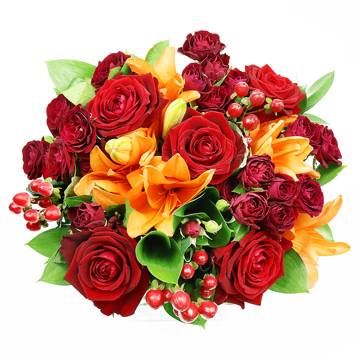 Viewed from a direct top-down angle on a bright white background, this compact, circular bouquet presents an opulent arrangement of autumnal reds and vibrant oranges held together by fresh greenery. Several large, fully bloomed deep red roses dominate the composition, their lush, velvety petals unfolding to reveal dense, romantic centers that draw the eye. Interleaved with these are bold orange Asiatic lilies, their trumpet-shaped forms offering dramatic contrast; some lilies lie open with stamens visible and textured pollen, while others remain in the poised, elegant shape of a bud, suggesting stages of life and longevity. Nestled between the principal blooms are clusters of small, dark burgundy spray roses whose tight, multi-petalled heads introduce depth and a plush, fabric-like surface. Bright hypericum berries-polished, spherical and ruby-red-are scattered through the bouquet, catching light and adding a playful, festive texture against the matte petals. The foliage is abundant but controlled: glossy, broad green leaves like ruscus or salal slip between flowers, their cool tones and smooth surfaces giving the arrangement breathing space and structural definition. Lighting is soft and even, chosen to reveal subtle petal textures and the bouquet's balanced roundness without harsh shadows. The imagined scent blends lilies' spicy-citrus top notes with the rounded, classic sweetness of roses. Perfect for anniversaries, romantic gestures, or seasonal centrepieces, this bouquet feels handmade with the quiet expertise one associates with florists around Canonbury Square and Upper Street.
