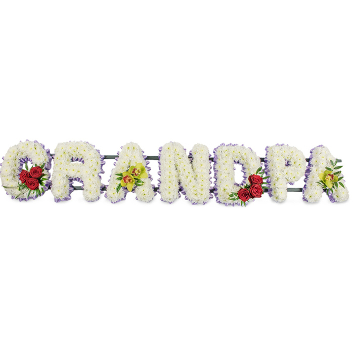 This image shows a carefully composed funeral flower tribute spelling GRANDPA in bold, upright capitals, the letters arranged in a straight horizontal line against a bright white background that intensifies every colour and contour. Each letter is completely covered with small white chrysanthemums, their rounded petals overlapping so closely that the surface looks thick and quilted, conveying softness and comfort in the midst of loss. Around the outer edges of the letters runs a slim trim of lavender-purple ribbon, just visible from the front and offering a delicate outline that helps the word stand out clearly, even from a distance in a Canonbury church or crematorium chapel. Thoughtfully placed accent flowers punctuate the white backdrop. In the open curve of the G, several deep red roses sit snugly among sprigs of glossy foliage, their rich hue and classic spiral form immediately drawing the eye. The first A to follow is adorned with a cluster of yellow-green orchids, some with subtle red speckling at the throat, giving a slightly exotic and refined character that might recall a grandfather's unique style or special interests. The D repeats the motif of the G with another cluster of red roses, visually balancing the tribute and reinforcing the message of devoted love. Finally, the last A at the far right carries another spray of the same yellow-green orchids, tying the whole piece together with quiet symmetry. Discreet horizontal bars and a dark frame support the letters from behind, ready for the tribute to be placed beside the coffin, at the front of a service, or at the graveside in Canonbury. The overall impression is one of peaceful purity, with touches of passion and respect woven gently through the design.