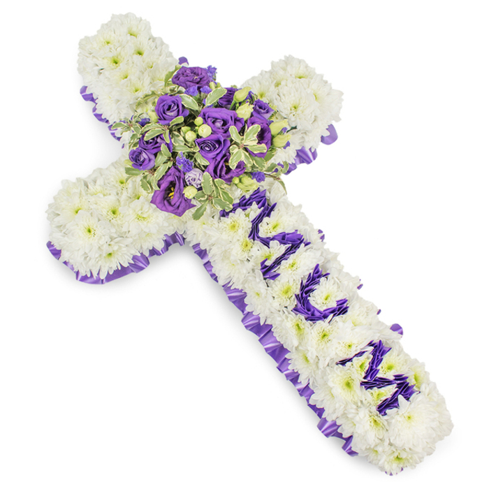 A large, solemn funeral cross formed from a dense blanket of small white chrysanthemum florets, each petal layered to create a soft, pillowy texture that reads as purity and calm. The entire outline of the cross is edged in a richly pleated purple satin ribbon, the ruffle providing a graceful, dignified frame that contrasts with the matte petals. Along the upright arm the name MUM is spelled in deliberate, stylised letters made from deep purple flower heads - likely lisianthus or compact spray chrysanthemums - their saturated colour deliberately set against the white to convey a deeply personal message. The central focal cluster, placed at the junction of the arms, is a lush composition of deep violet roses and paler lavender lisianthus, the roses' tight buds and the lisianthus' ruffled throats creating a layered, emotive centre. Variegated green foliage with lighter edges and darker centres weaves through the arrangement, adding depth and a suggestion of renewal; small round green berries are scattered through the spray, introducing gentle textural contrast. The arrangement is shown against a clean white background, allowing the cool tones - from snow-white to lilac and deep violet - to stand out with quiet dignity. A soft, powdery fragrance of roses and chrysanthemum seems almost perceptible, lending a gentle comfort. This bespoke memorial cross is suited to funeral services, wakes, or graveside tributes across Canonbury and neighbouring Newington Green, crafted with the restraint and attention to detail appropriate for a heartfelt farewell.