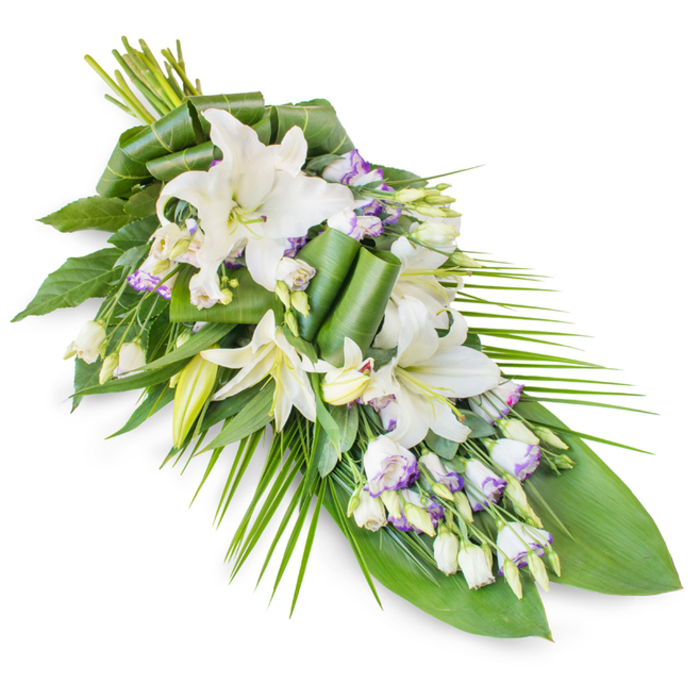 Set against a clean white background, this classic teardrop funeral spray unfolds in a diagonal sweep, its fuller cluster of flowers on the upper left softly narrowing to a pointed tip on the lower right. Dominating the arrangement are serene white oriental lilies, some fully unfurled with wide, satin-like petals, others captured as elegant buds poised to open. The open lilies display gently dusted yellow-green stamens, a subtle focal point within the purity of the blooms. Tucked between these larger flowers are sprays of lisianthus, their smaller, fluted blossoms mostly white but lightly washed at the edges with lavender and pale purple, lending a whisper of colour that feels as quiet as Canonbury's residential streets at dusk. Numerous buds and half-open lisianthus heads add a layered, textural quality, suggesting a story of a life made up of many chapters and memories. Supporting the flowers is an abundant base of greenery: broad, dark leaves lay down a deep green canvas, while long, slender palm fronds extend outward and slightly upward, especially on the right side, emphasizing the arrangement's elongated, flowing line. Some leaves are finely folded and rolled into graceful arcs, a signature touch that reflects the care and craftsmanship often seen from Canonbury funeral florists. The overall impression is of poised, solemn beauty, suitable for resting on a casket, dressing a memorial table, or being placed beside a framed photograph at a local service. With its clean palette and refined structure, this sympathy spray embodies peace, remembrance, and the quiet support of the Canonbury community in times of loss.