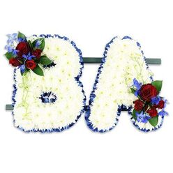 Carefully hand-crafted by Canonbury Flowers for families in and around Canonbury, this freestanding tribute spells the initials BA in bold, uppercase letters formed from hundreds of small, immaculate white chrysanthemums. The chrysanthemum heads are densely packed to create a soft, tactile surface that looks almost like carved cloud; their gentle texture invites a quiet touch while conveying a sense of purity and calm. Each letter is edged with a ruffled royal-blue satin ribbon that crisply defines the contours and offers a refined, ceremonial frame to the white base. The 'B' carries a lush accent on its upper left curve: several deep, velvety red roses in varying stages of bloom, paired with tall, cobalt-blue delphinium spikes that lend vertical contrast and a hint of coolness to the palette. Pale green tendrils and deeper green foliage weave through these flowers, adding movement and an organic finish. The 'A' mirrors this treatment with an equivalent cluster at its lower right, creating visual harmony across the pair. The two initials rest on a narrow, dark green horizontal stand that keeps them together as a single memorial statement. Photographed against a clean white backdrop and touched by soft, natural light - the sort of light you might find in a chapel on New River Walk or a small Canonbury chapel - the arrangement reads as dignified and intimate, a personalised floral message designed to honour memory and provide comfort.