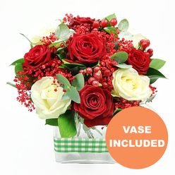 Against a crisp white backdrop, a carefully composed bouquet of red and white roses draws the eye with its rich colour and gentle symmetry, as though it has just been set down on a polished table in a Canonbury terrace. Full, velvety red roses are interlaced with creamy white blooms, each rose perfectly unfurled so the layered petals form soft spirals of light and shadow. Between them, tiny scarlet filler flowers resembling dyed baby's breath create a misty, textured layer, their small blossoms lending a sense of delicacy and intricacy to the design. Clusters of round, glossy red hypericum berries sit like bright beads among the petals, their shine adding a festive sparkle that feels at home during winter celebrations or romantic evenings along Upper Street. The arrangement is threaded with fresh greenery, including sprigs of silvery eucalyptus and other lush green foliage, which offers contrast to the rich reds and creams while suggesting a clean, herbal freshness. All of the blooms and leaves are gathered in a sleek, clear rectangular glass vase, allowing the neat stems to be seen and grounding the bouquet in a contemporary style that suits modern Canonbury apartments and classic period homes alike. Around the middle of the vase, a green and white gingham ribbon is snugly tied, introducing a touch of rustic charm that recalls local farmers' market stalls. In the lower right-hand corner, an orange circular graphic with the words "VASE INCLUDED" in white stands out clearly, signalling that this thoughtfully arranged floral gift arrives complete and ready to place as a centrepiece for anniversaries, birthdays, or quiet at-home celebrations.