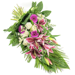 An elegant funeral sheaf is displayed on a clean white background, arranged on a gentle diagonal that carries the eye from the bound stems at the top left down to a soft cascade of foliage on the bottom right. At its heart, vivid Stargazer lilies unfurl, their petals a rich fuchsia-pink brushed with crisp white edges and scattered with dark wine-coloured speckles, giving the arrangement a sense of depth and emotion. Some lilies remain in bud, with pale green casings and blush hints of pink, promising a quieter beauty still to come. Nestled among them are bright magenta gerbera daisies, their flat, daisy-like faces adding modern vibrancy, while creamy white roses and softly ruffled white carnations offer a sense of purity and calm. Fine clusters of tiny white filler flowers flicker through the design like starlight, lightening the overall palette. Surrounding this core, lush greenery forms a supportive cradle: broad dark green leaves lay a structured base, feathery fern fronds soften the outline, and long, narrow leaves stream outward, accentuating the spray's elongated, teardrop form. The composition feels meticulously considered, much like the arrangements prepared for quiet services in Canonbury churches or intimate farewells in nearby Islington homes. The mood is solemn yet gently hopeful, a floral tribute suitable for resting beside a casket, adorning a crematorium service, or being delivered to a family home in N1. The interplay of vivid pinks, serene whites, and layered greens speaks of cherished memories, enduring love, and a respectful final goodbye.