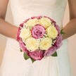 Bathed in bright, natural light, this Canonbury bridal bouquet glows with a heartfelt romance. The bouquet itself is a luscious circle of creamy lemon-yellow and vibrant fuchsia roses, each blossom bursting with freshness and expertly arranged to evoke classic beauty. The addition of subtle lavender and mauve tones among some petals introduces a graceful depth, while sprigs of baby's breath feather throughout-like a whisper of Canonbury's morning mist lifting over the New River. A few glossy green leaves peek from beneath, tying the composition to the borough's tranquil parks and doorstep gardens. The bride's gentle embrace frames the bouquet; her elegant white gown, with lacework reminiscent of centuries-old Canonbury villas, adds soft, swirling patterns to the scene. The softly blurred, neutral background grants the flowers their full radiance, their textures and colours tenderly celebrated by a local Canonbury florist. This bouquet feels infused with joy, promise, and the distinct personality of its neighbourhood-perfectly suited for those dreaming of a locally inspired, exquisitely personal wedding floral arrangement in Islington.