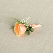 Bathed in gentle natural light, this boutonniere centres on a lush peach rose whose petals graduate from warm golden-apricot at the heart to a pale peach rim, creating a soft, luminescent depth that feels both refined and tender. Fine sprigs of gypsophila nestle around the bloom like a veil of tiny white blossoms, their delicate texture offering a whimsical, airy counterpoint to the rose's velvety presence. Curled glossy leaves and slender fern fronds arc around the stem, bringing verdant movement and a crisp green contrast that lifts the composition and frames the bloom with lively structure.

The stem is expertly wrapped in a matching peach satin ribbon, tied with a neat bow whose gentle sheen flashes as it rests against a neutral linen canvas; the finishing touch speaks to careful hands and an eye for proportion. There is a faint suggestion of scent - a soft, sweet rose perfume - and the whole piece evokes a tender, timeless feeling suited to weddings, milestone celebrations, or as a keepsake worn close to the heart. Prepared locally in Canonbury, Canonbury Flowers often crafts buttonholes like this for ceremonies at Canonbury Square and nearby chapels along Essex Road. Available for thoughtful local delivery, this boutonniere reads beautifully in photographs and embraces, offering a subtle emblem of love and quiet joy.