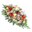 Photographed on a seamless white background, this large, traditional casket spray appears both structured and softly flowing, as if it has been carefully laid along the top of a coffin in readiness for a final farewell. The design is full and elongated, with its central section deepest in colour and volume, then gently tapering to more delicate points at each end. Dominating the heart of the spray are several deep red Oriental-style lilies, their velvety, star-shaped petals unfurled to reveal speckles and prominent stamens, creating dramatic points of focus that symbolise enduring love and courage. Encircling these are many roses in tones of cream, ivory, and pale blush pink, delicately scented and varied in openness, from small buds suggesting innocence and newness to broad, fully open blooms that speak of a long life cherished. Light pink spray carnations, with their ruffled petals and compact clusters, are threaded throughout to add softness and extra volume, while tiny white daisy or chrysanthemum florets bring a gentle brightness. Cool accents of blue-violet thistles introduce texture and contemporary flair, their spiky heads and steel-blue tones echoed by fine wisps of lavender-blue filler flowers that deepen the colour palette without overpowering it. All of this is securely cradled in a bed of lush, dark green foliage: large, glossy leaves give structure and depth, while smaller, feathery greens extend the spray's outline and enhance its sense of movement. The arrangement feels calm, respectful, and thoughtfully balanced, the kind of sympathy tribute a grieving family in Canonbury might choose for a funeral near Islington or along the quiet residential streets, created by a florist who understands the need for elegance and tenderness in moments of loss.