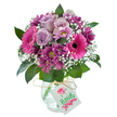 A striking floral arrangement, composed with passion and skill by local hands in Canonbury, stands out vividly against a pristine white backdrop. In its rounded embrace, soft lavender roses unfold beside exuberant fuchsia pink Gerbera daisies-each daisy's broad petals and bold centre a burst of energy, like children's laughter in Douglas Road's green spaces. Deep plum chrysanthemums nestle among the more vibrant blooms, their textured petals bringing a richness and subtle complexity reminiscent of Canonbury's hidden courtyards. Delicate clouds of white gyp dance through the bouquet, softening and brightening, while glossy green leaves peek through to frame the piece in natural elegance. The flowers are arranged in a charming, clear glass vase with a tactile, cracked-ice surface that catches and holds tiny flashes of light. Natural-coloured raffia is tied simply around the vase's neck, suspending a blank white gift tag-inviting messages of celebration or quiet gratitude. Radiating joy and appreciation, this Canonbury-inspired bouquet captures a moment's beauty, ready to delight recipients for birthdays, special occasions, or everyday gestures, embodying the neighbourhood's warmth and artistry.
