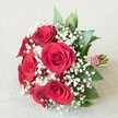 Resting gracefully upon a gentle cream-hued textured cloth-reminiscent of local Canonbury cafes and charming wedding venues-this lush hand-tied bouquet is a celebration of classic romance. Five to six deep red roses bloom at its centre, each blossom's velvety petals swirling in tight, elegant spirals that echo enduring love and sophisticated style deeply rooted in the Canonbury community. Scattered throughout, feather-light clusters of pristine white baby's breath (Gypsophila) offer a dreamy contrast, lending the bouquet a soft, ethereal aura that balances the powerful red. Sprigs of freshly gathered green foliage peek from behind the blooms, conjuring the scent of morning strolls along Canonbury's tree-lined streets. The bouquet's stems are neatly gathered and bound with a crisp red and white striped ribbon, adorned with a string of delicate white pearls-a refined detail that nods to both tradition and fashion. Bathed in soft, even light, every petal, leaf, and pearl is illuminated, showcasing the bouquet's freshness and expert arrangement. Perfect for weddings, anniversaries, or romantic gestures, this Canonbury creation embodies the beauty of local craftsmanship and stands as an ideal subject for articles exploring bridal bouquets, heartfelt gifts, or timeless floral symbolism within the North London area.