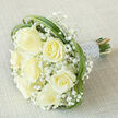 Seven creamy ivory roses anchor this elegant hand-tied bouquet, each bloom shown in a slightly different stage of opening so the composition feels alive and generous. Those broad, silky petals are cushioned by delicate clusters of white Gypsophila - baby's breath - which drift between the roses like little puffs of cloud, lending a soft, weightless texture. Bright green loops of bear grass weave through and around the flowers, providing sculptural movement and a fresh, contemporary silhouette that lifts the eye across the arrangement. The stems are bound firmly into a neat handle, wrapped in lustrous silvery-white satin; tiny, pearlescent beads run in multiple rows along the ribbon, introducing a refined, tactile detail that suggests traditional bridal refinement.
Laid diagonally on a light beige, linen-textured surface, the bouquet is presented in serene, diffused light that accentuates petal contours and the satin's cool sheen. One can almost sense the faint, sweet scent of roses and the cool touch of satin beneath the fingers. This composition reads as a choice of quiet celebration - for weddings, anniversaries, or gentle remembrances - and is the kind of arrangement brides on nearby Essex Road and Upper Street often select when they want classic simplicity with a contemporary twist. The image emphasises craftsmanship, soft romance, and the reassuring calm of thoughtful floral design.