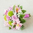 This carefully composed bouquet, created by experienced Canonbury florists, lies angled atop an elegant light beige linen-its palette a thoughtful tribute to the area's serene character. Velvety pink roses at various stages of opening provide the romantic heart of the arrangement, while apple-green button chrysanthemums offer a lively pop of colour, their round, tightly-packed forms contributing both texture and freshness. Delicate pink and blush alstroemeria, delicately speckled on their inner petals, are artfully woven between the main blooms, bringing a gently exotic flair evocative of Canonbury's artistic community. Wisps of cloud-white gypsophila fill the interstices, lending lightness and a subtle hint of countryside air, as seen in the lush parks nearby. The entire bouquet is encircled by glossy green foliage, its shapes and shades enhancing depth and serving as a perfect visual frame. At the base, the exposed natural stems are neatly secured with a magenta-pink satin ribbon, adding a final touch of elegance reminiscent of Canonbury's unique blend of heritage and modern style. Illuminated by soft, diffuse lighting, every hue and contour stands out-each petal, leaf, and cluster bathed in a sense of freshness and attentive craft. Ideal for weddings, heartfelt tributes, or as a radiant centerpiece, this bouquet embodies the welcoming spirit and floral artistry that defines Canonbury Flowers, ready to brighten any home or local occasion.