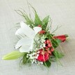Bathed in soft natural light, this elegant and heartwarming floral piece rests on a subtly woven linen fabric, instantly evoking the relaxed yet sophisticated ambiance of Canonbury. A stunning white lily anchors the design, its petals fully open and sprinkled with fine brown-orange flecks, while a classic red rose offers depth and passion at its side-both blooms echoing the timeless beauty found in the gardens off Canonbury Road. These central flowers are enhanced by delicate clusters of white baby's breath, giving the arrangement a gentle, cloudlike texture, and by shiny red berries that pop with colour and cheer. A single pale green lily bud stretches gracefully, whispering of future blooms and hope, while mixed foliage-ranging from dainty fern tendrils to broader, lustrous green leaves-cradles the flowers in a lush embrace. The bouquet is skillfully gathered and finished with a rich satin red ribbon, imparting a sense of care and refinement. Whether created to accompany a wedding celebration, as a bridesmaid's bouquet, or as a thoughtful gesture, this arrangement beautifully embodies the spirit of Canonbury-charming, classic, and quietly joyful, available for delivery to every special corner of Islington.