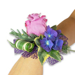 This wrist corsage reads as a small, modern love letter in flowers: at its centre a velvety lavender-pink rose unfurls in a soft spiral, petals edged a hair darker with a faint, dewy sheen, inviting the fingertips. Beside it, three clusters of indigo-to-midnight hydrangea form luminous pockets of deep blue-purple, each tiny floret showing a pale bluish heart that seems to catch evening light. Glossy, variegated ivy frames the blooms with dark green centres and creamy yellow edges, while long, silvery-green sprigs-think eucalyptus or lavender foliage-sweep gently behind the composition to add a breathable, pastoral texture and a faint, herbaceous scent. A sculptural wide leaf, striped white and green, is rolled into a tight spiral that gives the piece a contemporary architectural twist, balancing the softness of the rose. Underneath, a layer of open-weave deep purple mesh lifts and separates the flowers, its lacy shadow amplifying the hydrangea's richness and adding a whisper of sparkle like a gown's beadwork. The overall balance is tactile: silky rose, papery hydrangea, crisp ivy and feathery greens that together feel cool and lightly scented-an impression of an early summer garden after rain. Composed on a fair-skinned wrist and photographed against a clean white backdrop, the colours pop with refined clarity. As a florist who has placed corsages for Canonbury celebrations from Canonbury Square to New River Walk, I imagine this worn for bridesmaids, proms, or anniversaries-an elegant, contemporary accent that reads as both romantic and quietly confident while remaining comfortably local and fresh.
